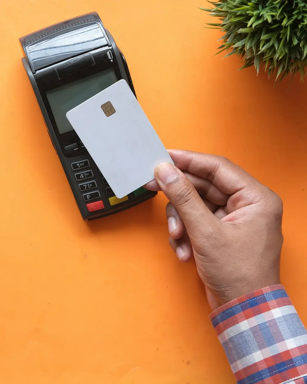 A blank white bank card held against the reader of a payment terminal on a desk.