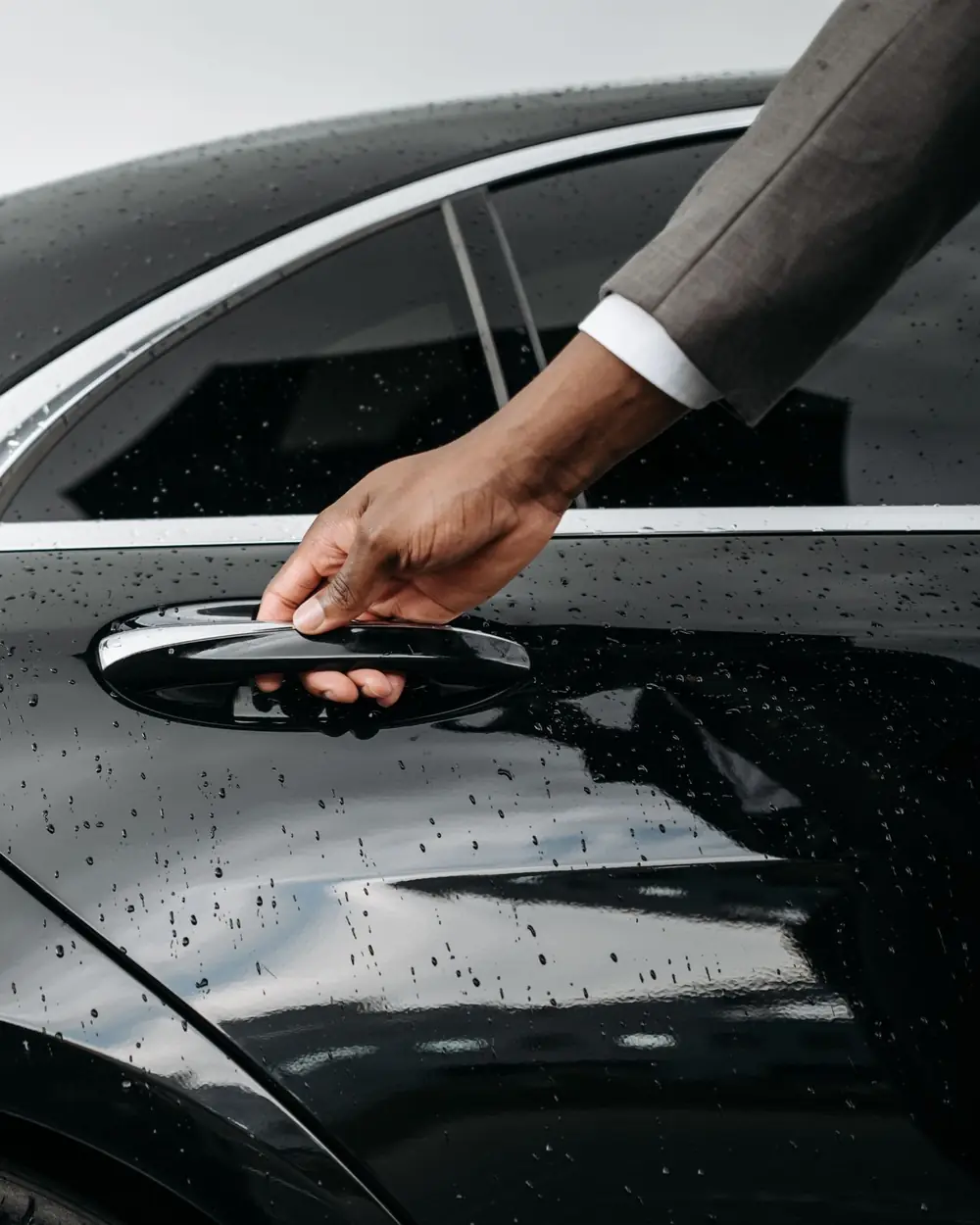 A hand on the rear passenger door handle of a dark sedan at the kerb.