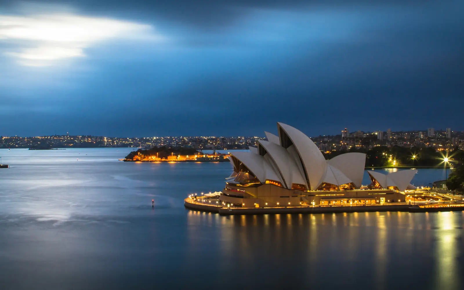 Sydney Harbour at dusk, the lit Opera House on the point and the city beyond it.